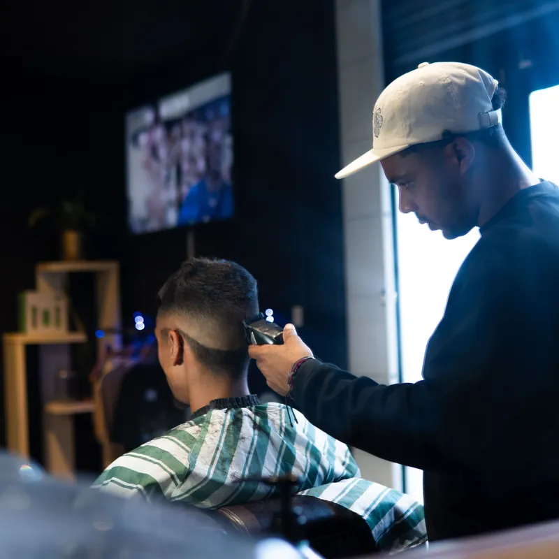 A client in The Medallion's green striped cape while the barber works on his fade